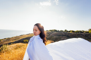A young attractive Asian woman wrapped in a white blanket and and enjoys the mountains and the sea