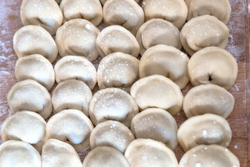 The raw dumplings were placed on a wooden cooking board, sprinkled with flour. The filling is...