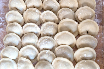 The raw dumplings were placed on a wooden cooking board, sprinkled with flour. The filling is minced meat, potatoes, cheese or cottage cheese. A semi-finished product, ready for cooking.