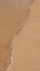 Tranquil Beach Scene with Footprint in Sand, Gentle Wave, and Clear Blue Sky on a Sunny Day.