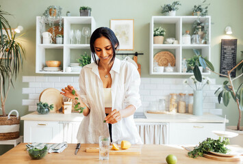 A young attractive woman makes delicious fresh lemonade and sniffs lemon and mint