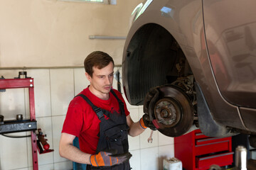 a mechanic stands by a car in a car service center. master repairs car brake discs and pads