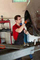a mechanic stands by a car in a car service center. master repairs car brake discs and pads