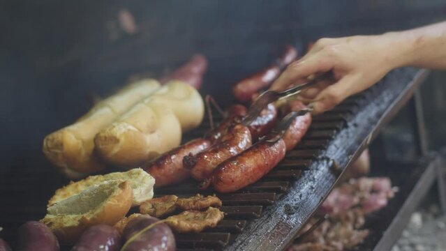 Asador da vuelta un chorizo y saca otra tira de chorizos de la parrilla. Parrillada, Asado.