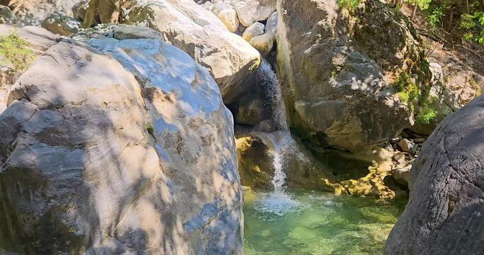 Small turquoise waterfall with crystal clear green pond in Samaria Gorge, Crete, Greece, large white boulders around. 