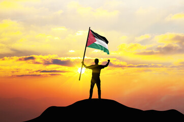 Palestine flag being waved by a man celebrating success at the top of a mountain against sunset or sunrise. Palestine flag for Independence Day.