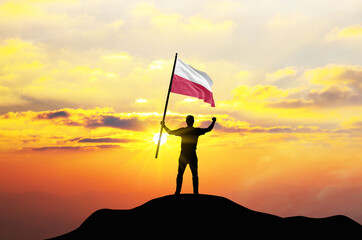 Poland flag being waved by a man celebrating success at the top of a mountain against sunset or sunrise. Poland flag for Independence Day.