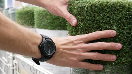 Close-up of many artificial turf rolls on the market and a man choosing one