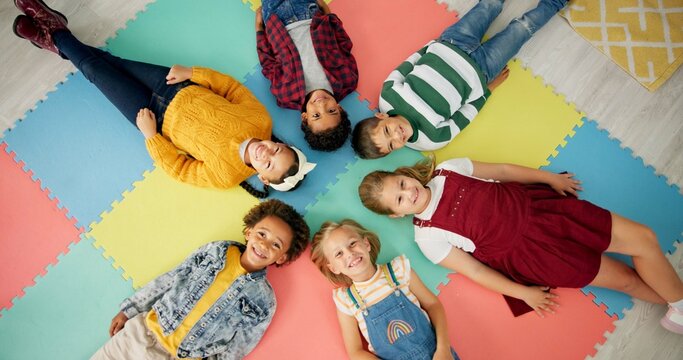 Kids, lying down and circle in school with top view for relax, fun and classroom on colourful foam mat. Group, children and happy on floor for education, learning and knowledge with game for bonding
