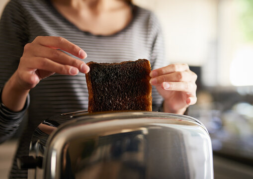 Hands, woman and burnt toast for breakfast in kitchen as cooking disaster, fail and accident as mistake in morning. Frustrated, person and black bread for unhealthy, electrical problem or safety