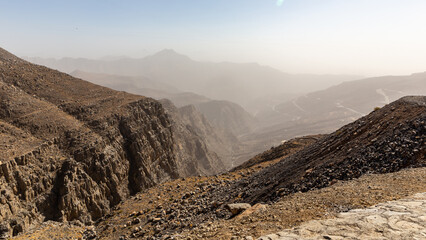 Rocky and barren Hajar Mountains mountain range with haze on the horizon seen from Jebel Jais Viewing Deck Park, United Arab Emirates.