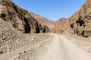 Gravel dirt road through rocky limestone Hajar Mountains and cliffs in United Arab Emirates, barren desert vegetation.