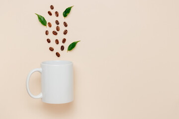 White mockup mug with coffee beans and green leaves on beige background, top view. Coffee mug for...