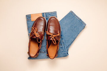 Men's fashionable outfit top view. Blue jeans with leather moccasins shoes or loafers on beige background, casual look