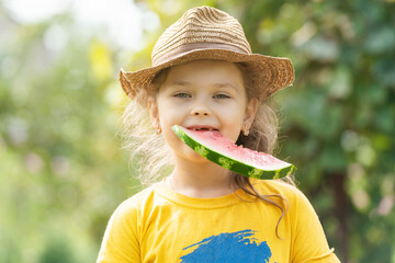 Little girl in a hat eats a ripe red watermelon