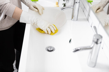 Close-up shot of woman in rubber gloves cleans sink and faucet with a rag and spray in the...