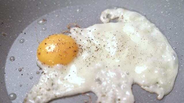 the cook peppers and salts fried eggs in a frying pan on the stove while cooking breakfast