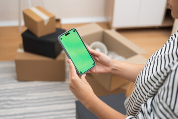 Seamless Move-In: A woman holds a smartphone with a green screen, set against a blur of cardboard...