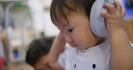 A asian baby child toddler girl wearing headphones listen music and looking at something. daughter...