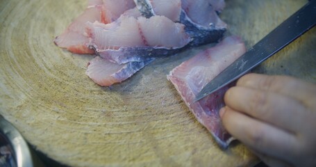 A person is cutting fish on a wooden cutting board. The fish is cut into small pieces. Concept of...