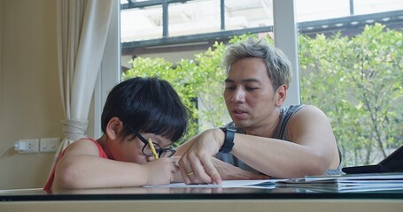 happy family cute Asian child boy with eyeglasses studying doing homework with father helping teaching his son sitting together at living room, education learning home school