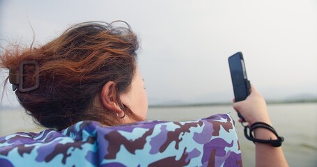 A asian woman is sitting on a longtail boat wearing life jacket looking out nature river lake at...