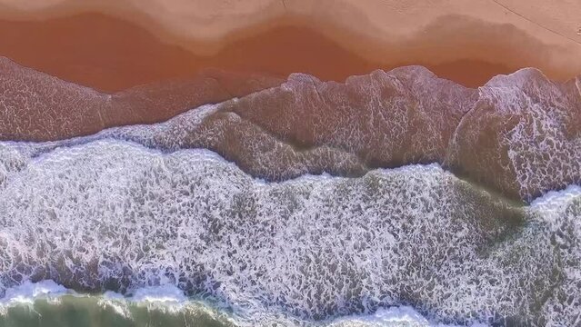 Ondas do mar quebrando na areia fazendo espuma. V&iacute;deo a&eacute;reo em &acirc;ngulo azimutal feito por drone em uma manh&atilde; do litoral da Bahia, Brasil.
