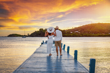 A beautiful honemyoon couple on a pier enjoys the tropical sunset in the Caribbean Sea, Antigua and Barbuda island