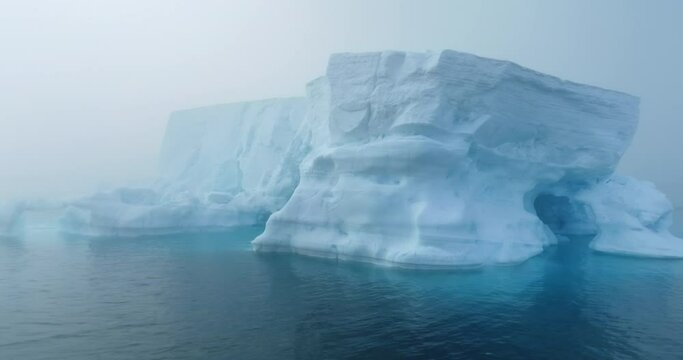 Large iceberg floating in polar ocean in foggy mist day in Antarctica. Tabular huge high ice glacier melting ice cave at wild nature environment. Arctic winter landscape at global warming problem.