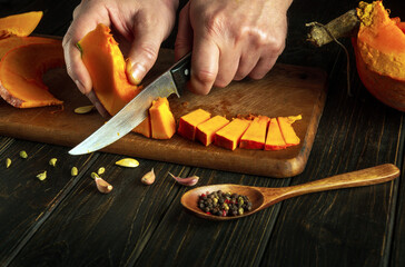 Slicing pumpkin with a knife in the hands of a man on a wooden board for preparing a vegetarian...