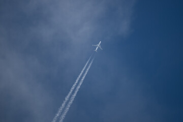 Ein Flugzeug fliegt durch den blauen Himmel und macht Kondensstreifen