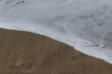 Foam from wave crashing on dark brown beach sand