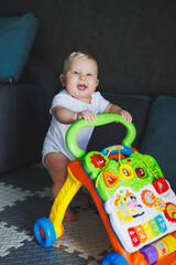 A blue-eyed baby learns to walk with the help of a walker. The baby is developing and learning to...