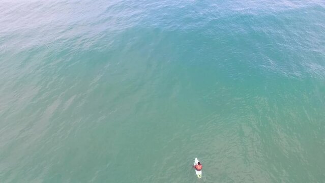 Imagem a&eacute;rea de surfista solit&aacute;rio esperando a onda perfeita no mar de Taipu de Fora, Bahia, Brasil. Drone filmando homem com prancha no mar azul.