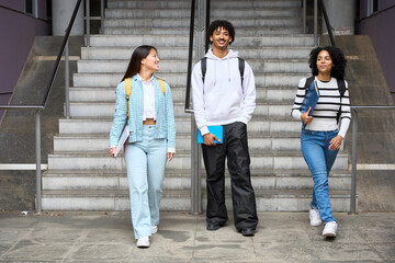 Three young students are walking up a set of stairs, each carrying a backpack