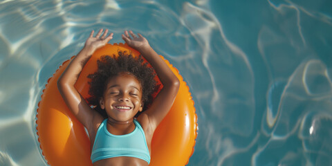Aerial view of a happy girl with curly hair lying on an orange float in a light blue pool, the girl smiles and enjoys a sunny day outdoors.