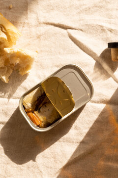 Still life of Portugese tinned sardines with olive oil served with crusty bread loaf and port tonic and lime.