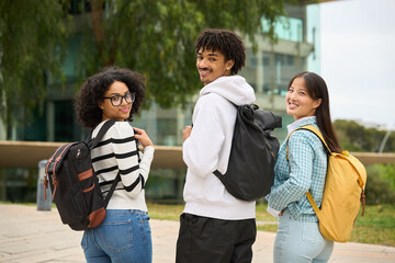 Three young students are standing together, each carrying a backpack