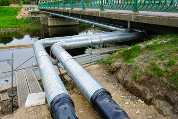Installation of a new heating pipeline in a galvanized metal casing under the bridge over the river
