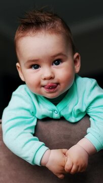 Playful beautiful kid with funny hair standing on the chair. Lovely toddler showing tongue and smiling. Low angle view. Vertical video