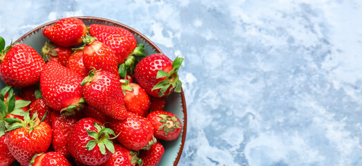 Bowl with fresh strawberries on blue background