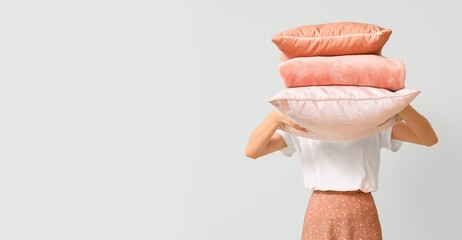 Woman holding soft pillows on light background with space for text