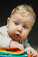 Fototapeta premium A small child in a white bodysuit is learning to crawl on a clean, heated floor. Home photo of a cute blue-eyed baby.