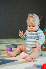 Fototapeta premium A small child in a white bodysuit is learning to crawl on a clean, heated floor. Home photo of a cute blue-eyed baby.