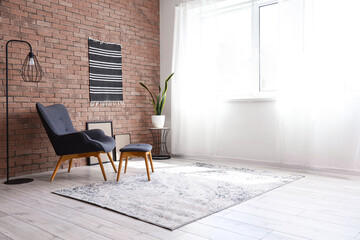 Stylish grey armchair with footstool near window in light living room