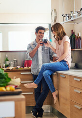 Happy, couple cooking and drinking together for bonding in kitchen over romantic meal preparation at home. Excited, man and woman with wine glasses and cutting board for nutrition and healthy food