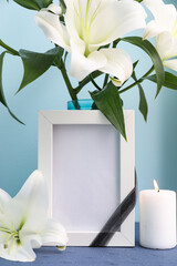 Blank funeral frame, burning candle and vase with lily flowers on table near color wall, closeup