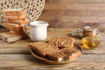 Plate of toasts with peanut butter and bowl of honey on wooden background