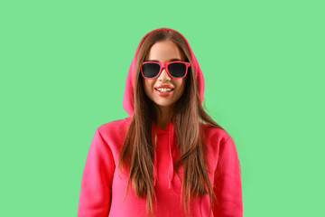 Young woman in hoodie with sunglasses on green background