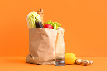 Paper bag with different fresh vegetables, fruits and bottle of water on orange background